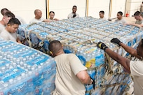 Airmen wrap and tighten cargo straps around a large pallet of water and supplies for transport.