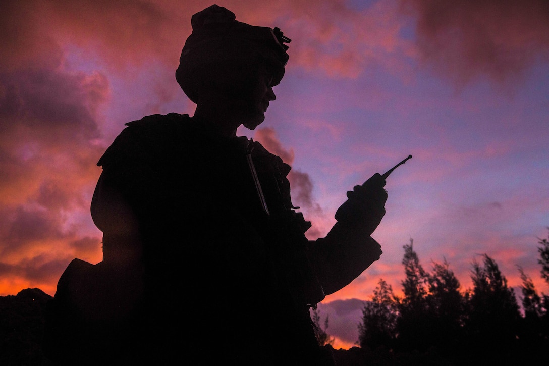 A Marine, shown in silhouette, holds a radio.