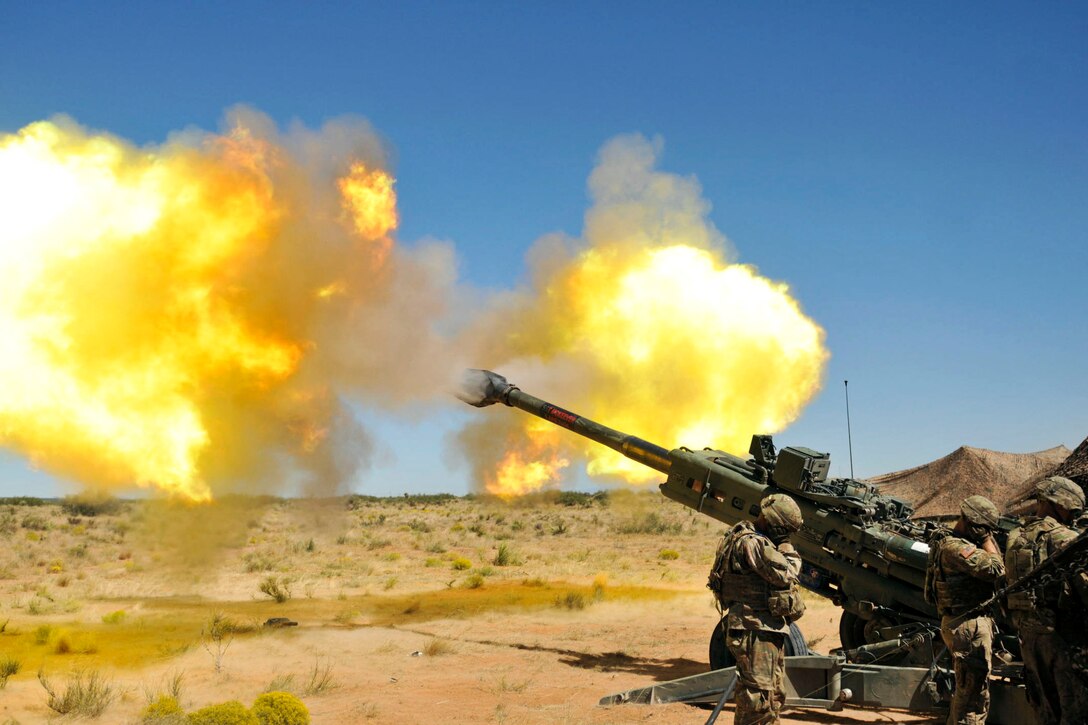 Soldiers cover their ears as a howitzer fires.