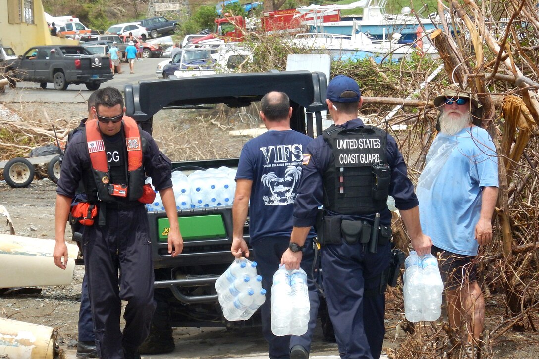 Members of the Coast Guard carry water near a small vehicle.
