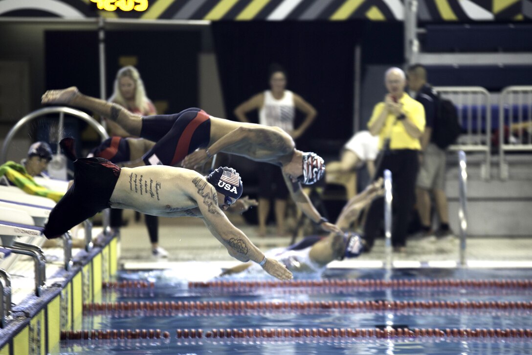 Two people dive into a pool from starting blocks.