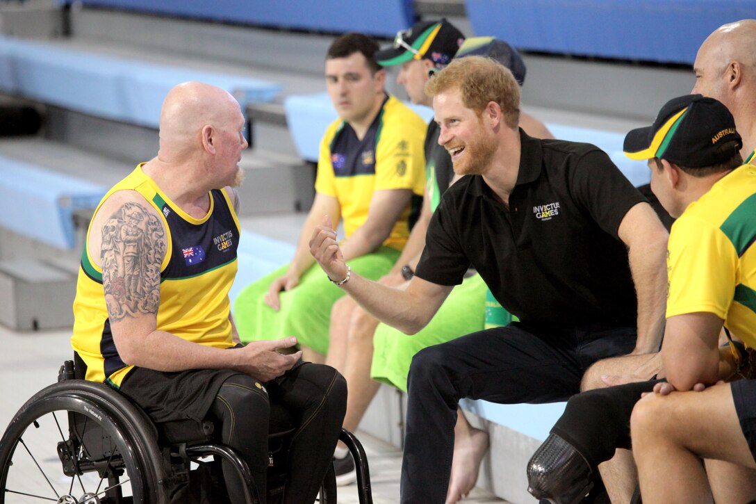 Prince Harry sits on bleachers with athletes.