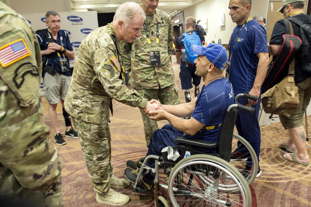 An army general leans over to shake the hand of a person in a wheelchair.