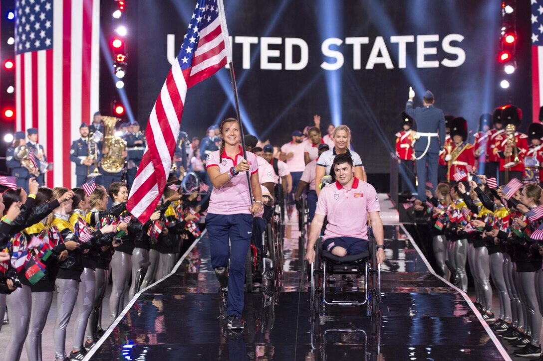 A person carrying the American flag and a person in a wheel chair lead a team on stage.