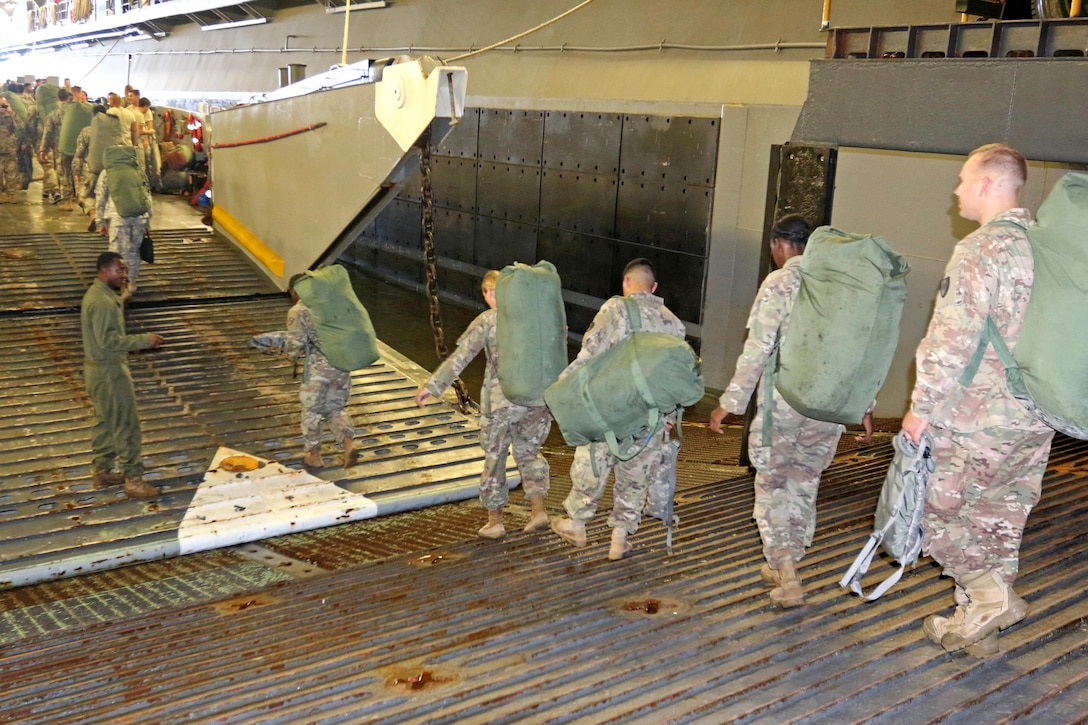 A line of soldiers walk on a ramp to board an amphibious ship.