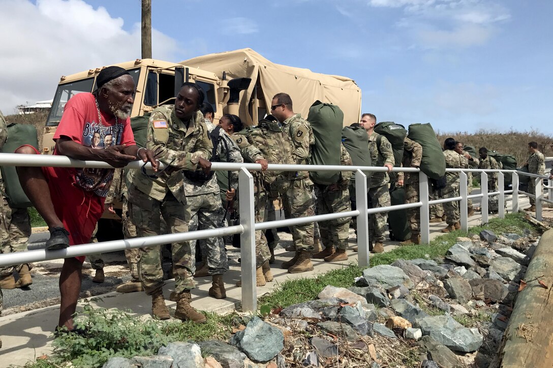 A civilian leans on a fence with a group of soldiers nearby.