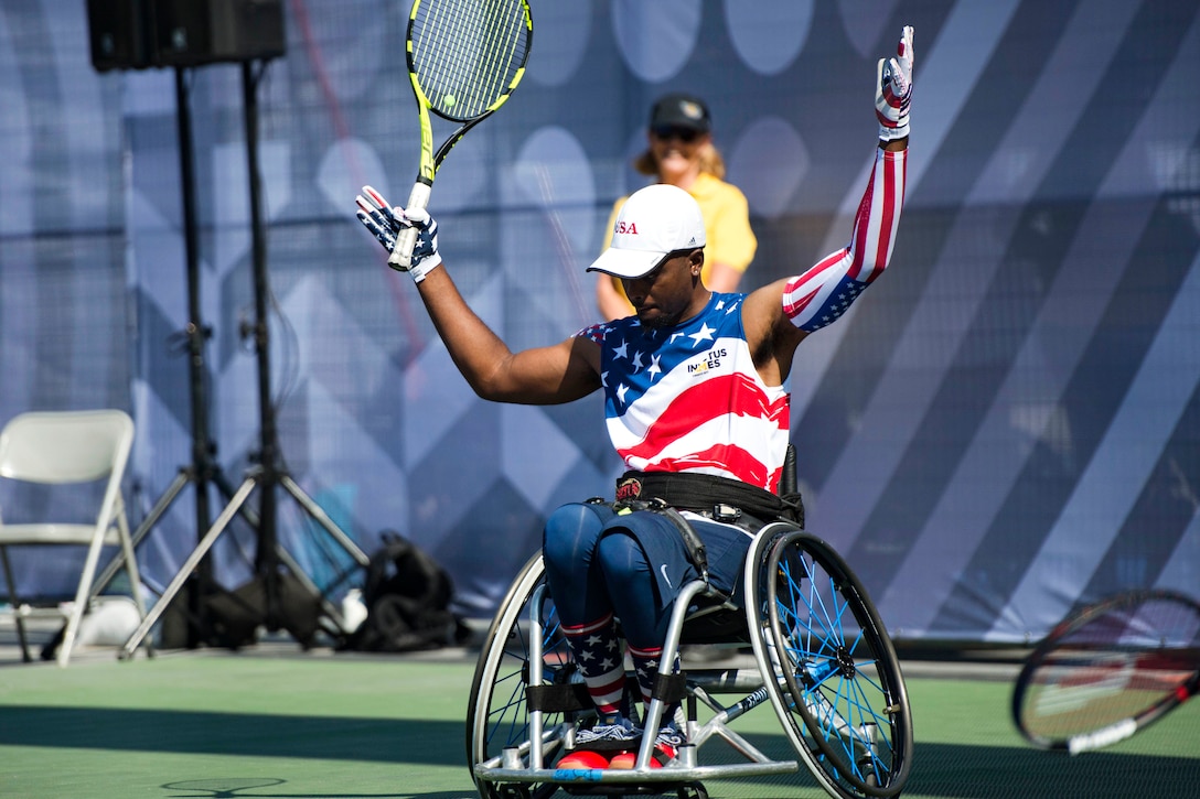 A wheelchair-bound athlete with a tennis racket holds his hands over his head.