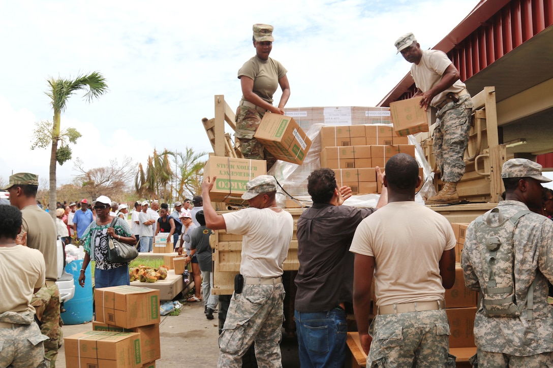 Soldiers hand boxes of food off the back of a truck to other soldiers.