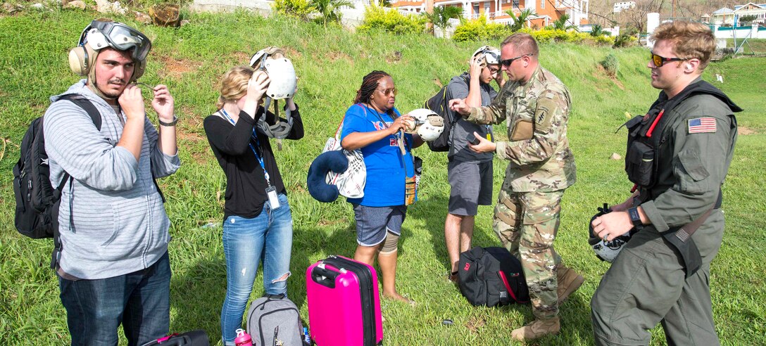 Two service members help civilians put on protective head gear.