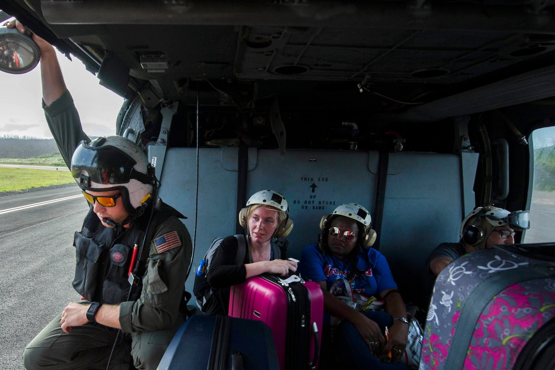 A service member and civilians sit in a helicopter during take-off.