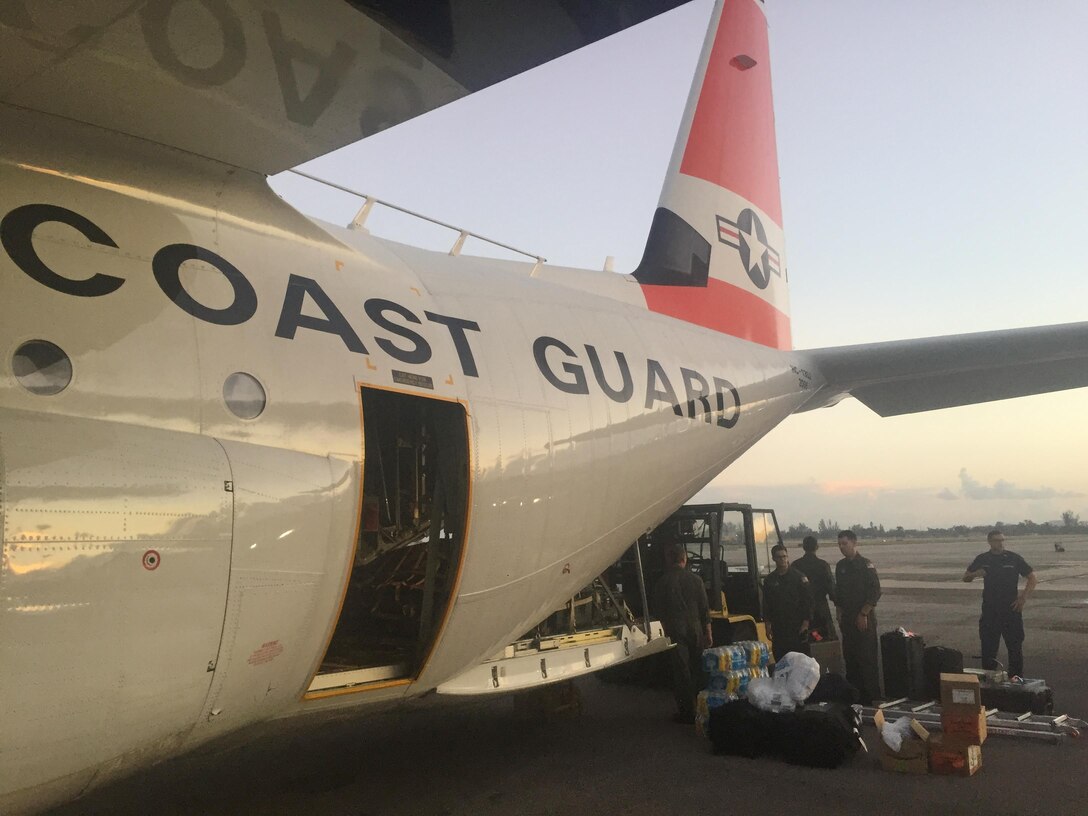Coast Guard members load relief supplies onto an aircraft .