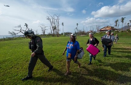 A U.S. Navy Sailor guides U.S. citizens out of an MH-60S Sea Hawk helicopter during relief efforts in the wake of Hurricane Maria.