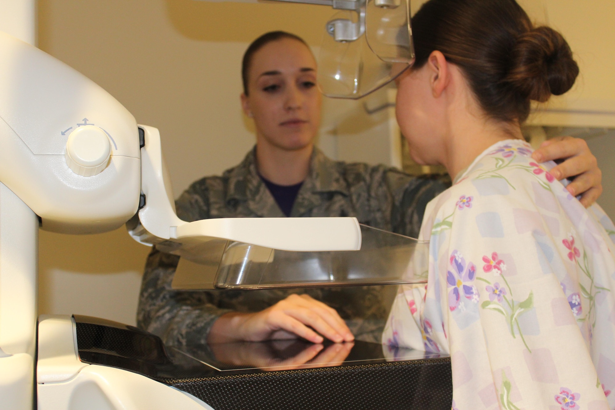 88th Medical Group radiology technician Senior Airman Katie Bryan, simulates having a mammogram while mammography course instructor SSgt Lauren Le’vey, explains the mammogram process. A mammogram should take no more than 20 minutes and radiologists will look for potential signs of breast cancer such as lumps or tumors. (U.S. Air Force Photos/Stacey Geiger)