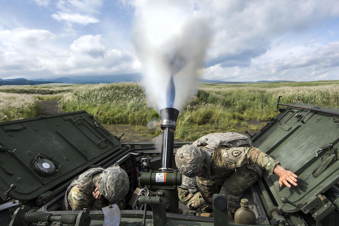 Soldiers crouch as a mortar system fires.