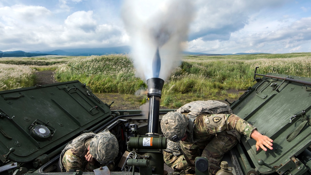 Soldiers crouch as a mortar system fires.