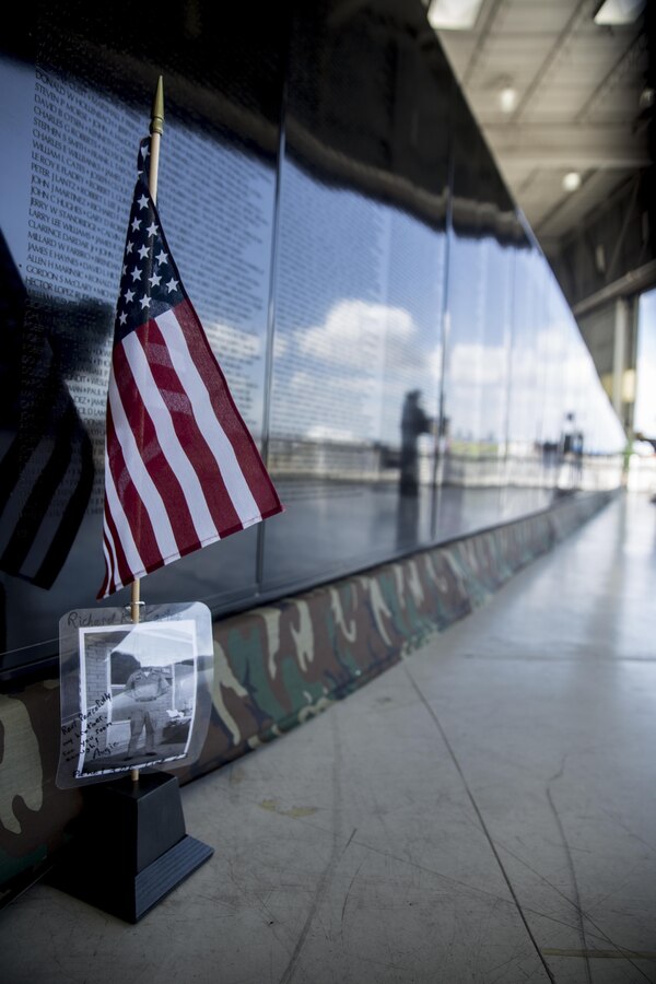 A picture of Sgt. Richard Carter, a soldier who died during the Vietnam War, rests in front of the Mobile Vietnam Memorial Wall, also known as the AV Wall, during the 2017 Marine Corps Air Station Miramar Air Show at MCAS Miramar, Calif., Sept. 22. Carter’s brother, Augie Anderson, is an AV Wall volunteer and placed the flag and photograph as a way to remember Carter, who died Nov. 19, 1967.  Anderson wrote “Rest peacefully my brother, see you soon enough!” (U.S. Marine Corps photo by Sgt. Lillian Stephens/Released)