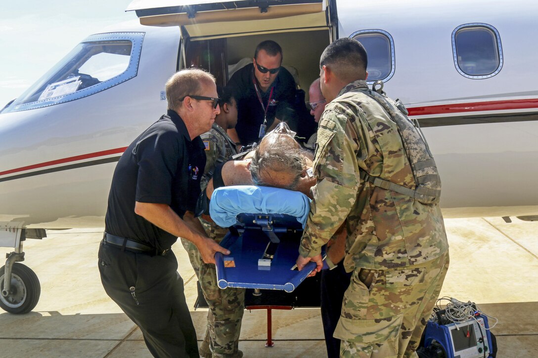 Soldiers help board a patient on a stretcher into an airplane.