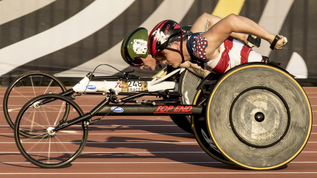 A Marine speeds past a British athlete in a wheelchair track event.