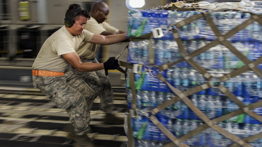 Two airmen pull a pallet of bottled water inside an aircraft.