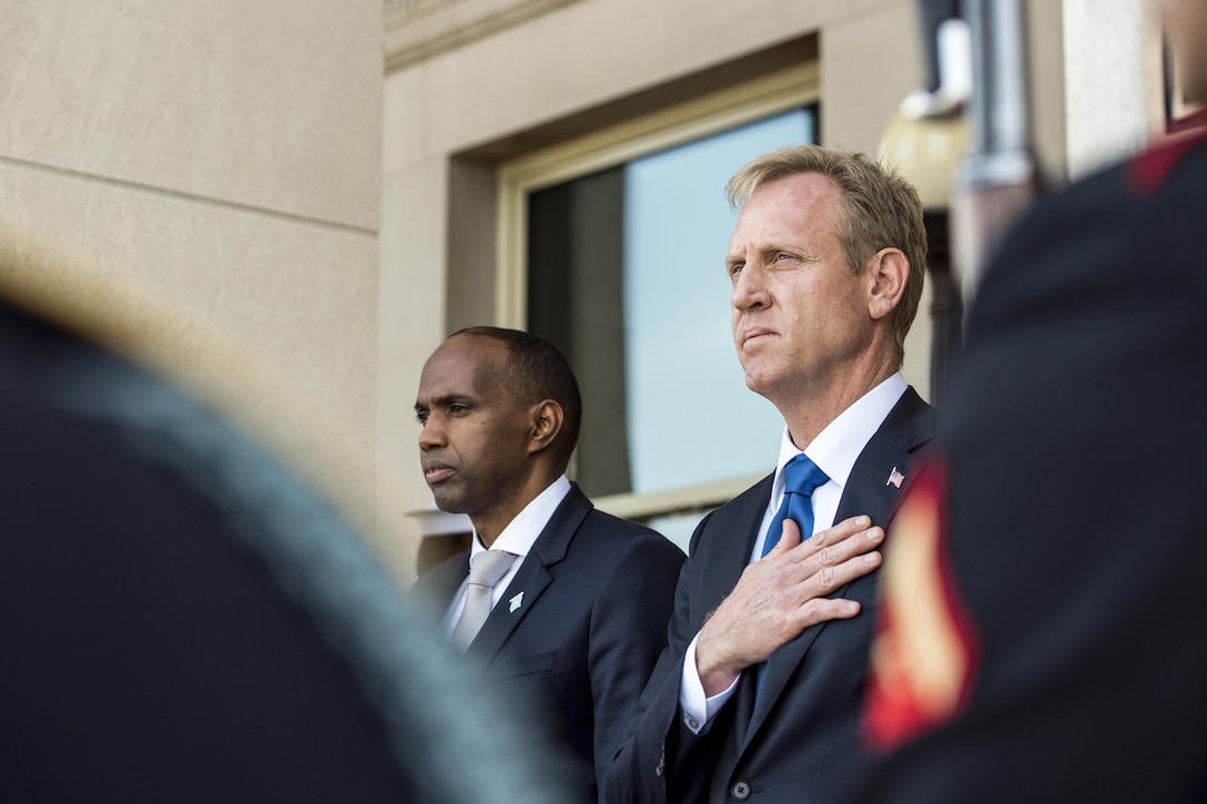 Deputy Defense Secretary Pat Shanahan holds his hand over his heart while standing with another official.