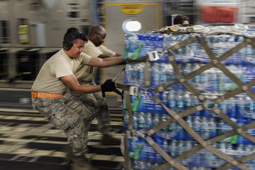 Two airmen pull a pallet of bottled water inside an aircraft.