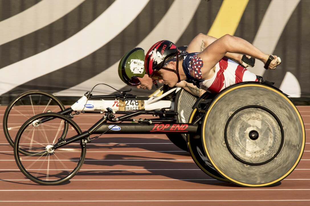 A Marine speeds past a British athlete in a wheelchair track event.