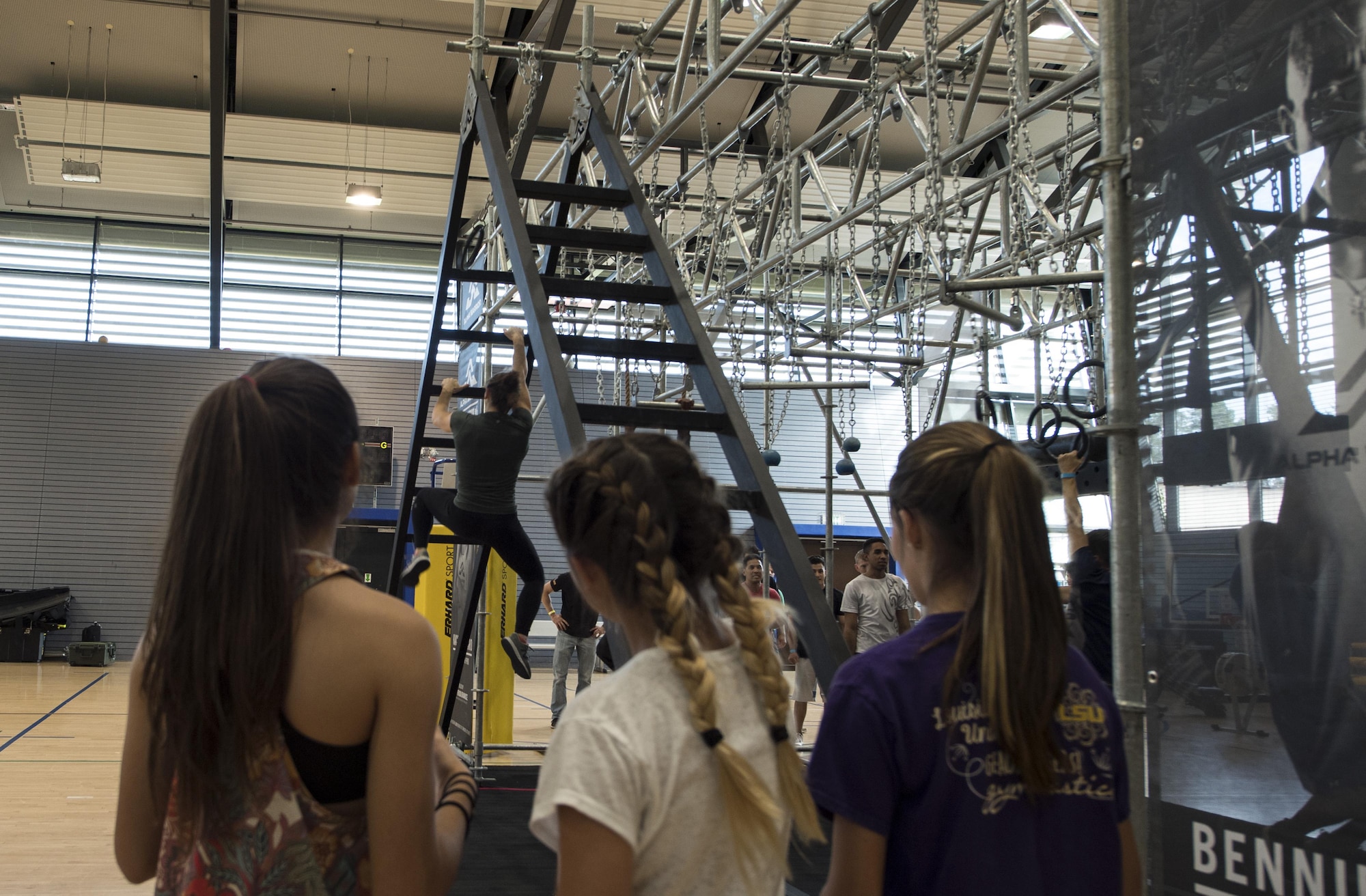 Barclay Stockett, Alpha Warrior pro, demonstrates how to climb and descend the ladder portion of the Alpha Warrior’s Battle Rig obstacle course to three young girls during the Alpha Warrior Tour on Ramstein Air Base, Germany, Sept. 22, 2017. The first day of the tour provided Department of Defense cardholders 13 years and older an opportunity to test their skills on the obstacle course. (U.S. Air Force photo by Senior Airman Tryphena Mayhugh)