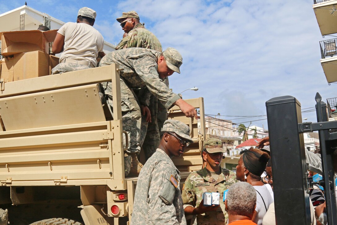 Guardsmen behind and on a military vehicle had supplies to civilians.