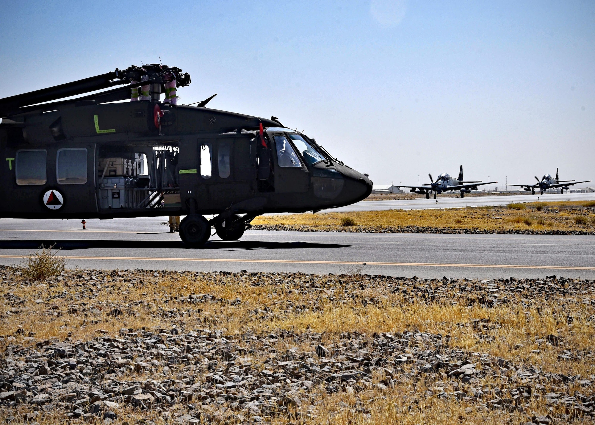 An Afghan Air Force UH-60 is towed as two AAF A-29s taxi for take-off Sept. 18, 2017, at Kandahar Air Field, Afghanistan. The UH-60 was the first to arrive in Afghanistan as part of modernization efforts to transition the AAF to a more sustainable and modern helicopter fleet. (U.S. Air Force photo by Tech. Sgt. Veronica Pierce)