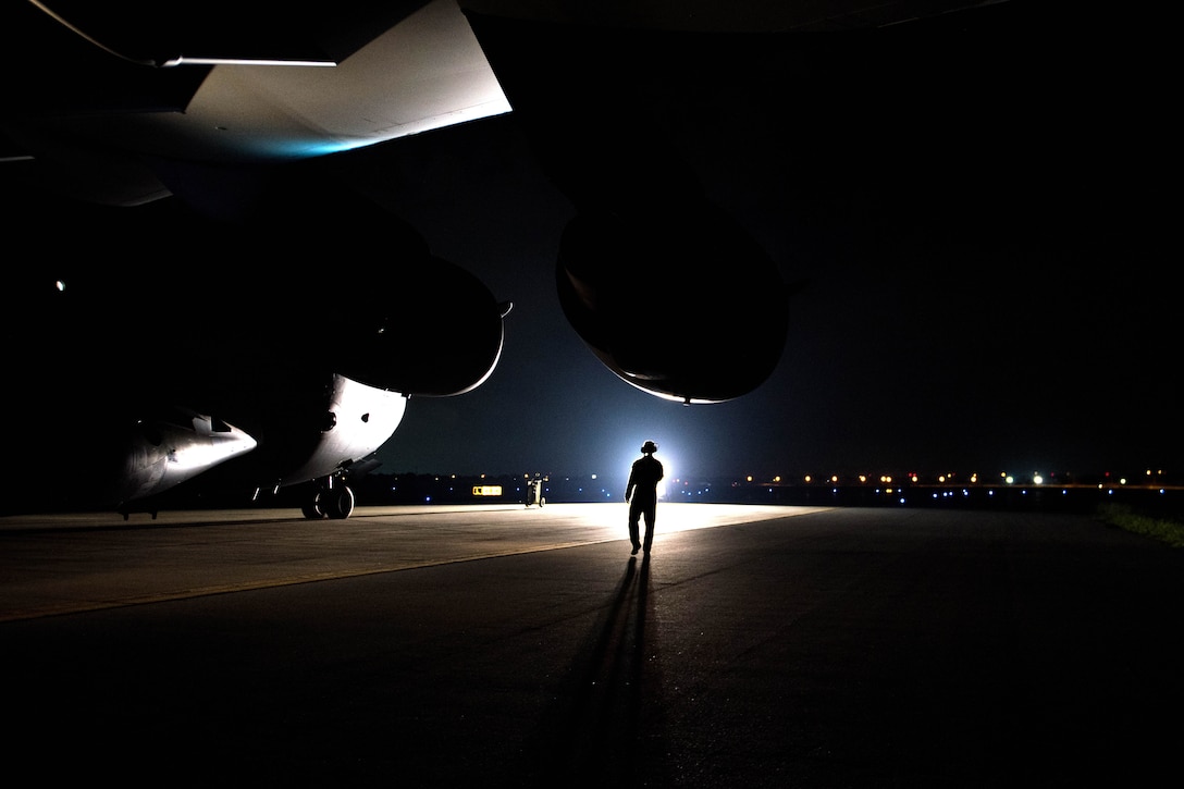 An airman stands in a beam of light near an aircraft.
