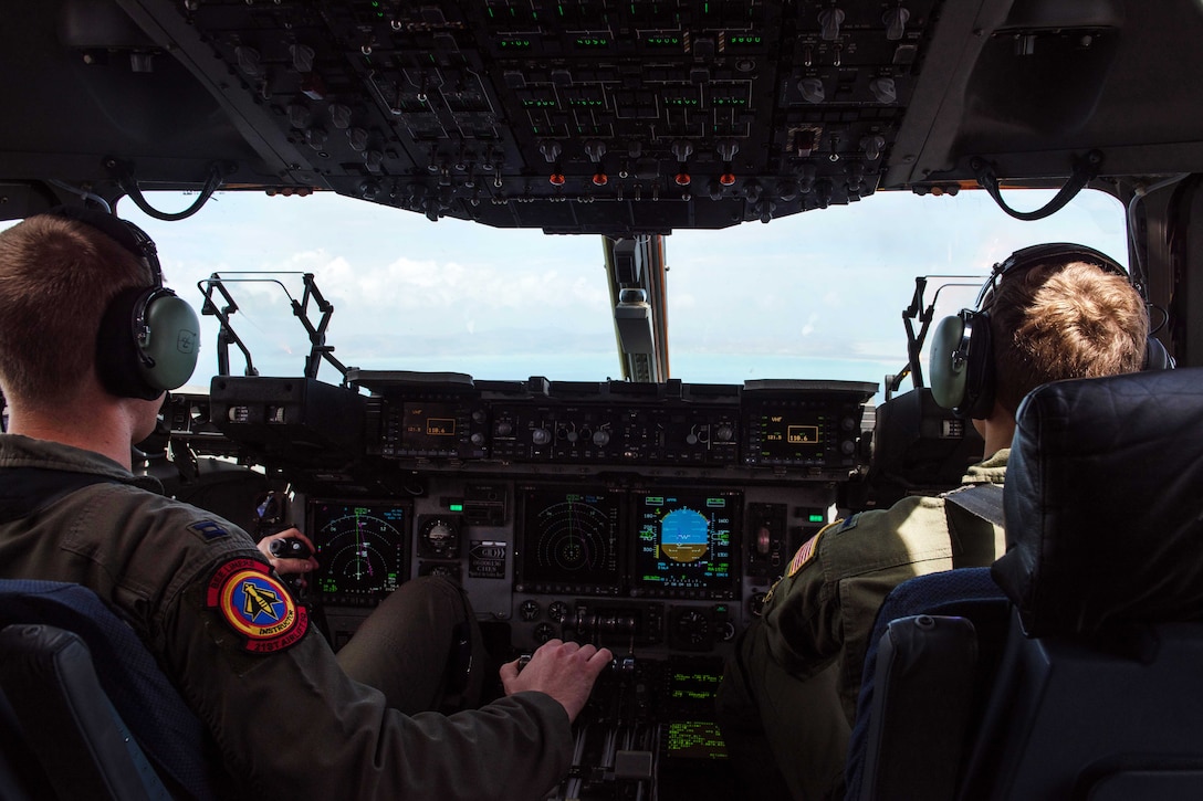 Two pilots sit behind the controls of an aircraft with sky through the windshield.