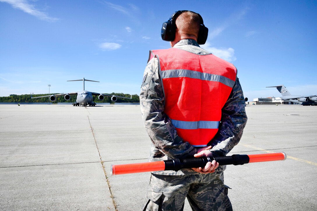 An airman stands with a reflective vest and hearing protection.