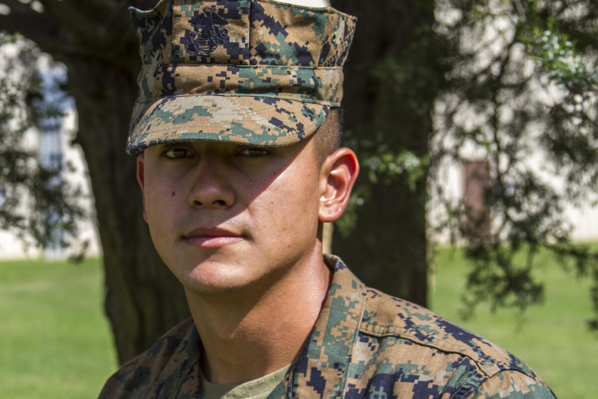 Close shot of a Marine looking at the camera while standing in front of a tree.