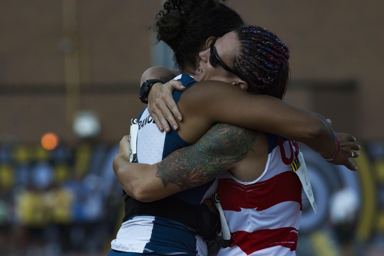 Retired Marine Corps Cpl. Sarah Rudder, right, hugs a French athlete after competing in the women's 100-meter dash.