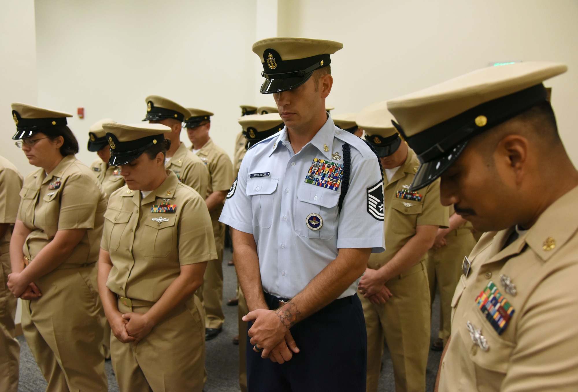 Master Sgt. Joshua Anderson, 81st Training Support Squadron Military Training Leader School instructor supervisor, and members of the Center for Naval Aviation Technical Training Unit Keesler bow their heads in prayer during the CNATTU Keesler Chief Petty Officer Pinning Ceremony at the Roberts Consolidated Aircraft Maintenance Facility Sept. 15, 2017, on Keesler Air Force Base, Mississippi. The six-week long Navy Chief Petty Officer Courses held at Keesler and the Naval Construction Battalion Center in Gulfport, Mississippi included four Air Force members, which is the first time Keesler Air Force members have gone through this process. The course is meant to enhance leadership skills and to strengthen the Navy-Air Force enlisted leadership relationship on Keesler. (U.S. Air Force photo by Kemberly Groue)