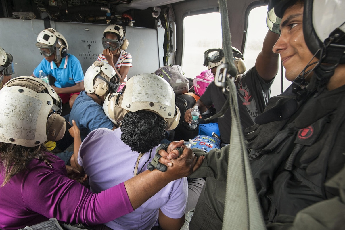 A sailor holds the hand of a hurricane victim during a helicopter ride.