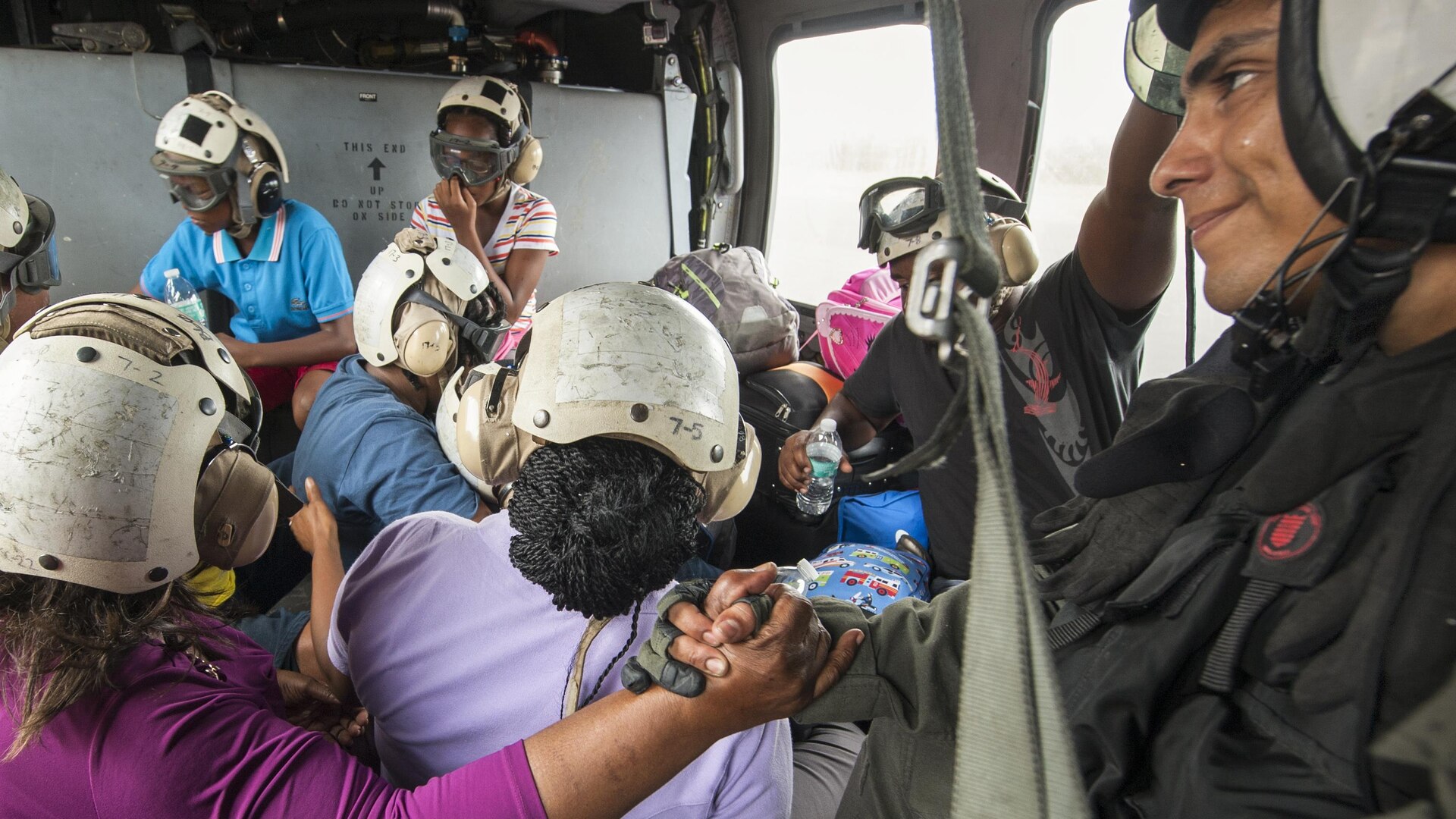 A sailor holds the hand of a hurricane victim during a helicopter ride.
