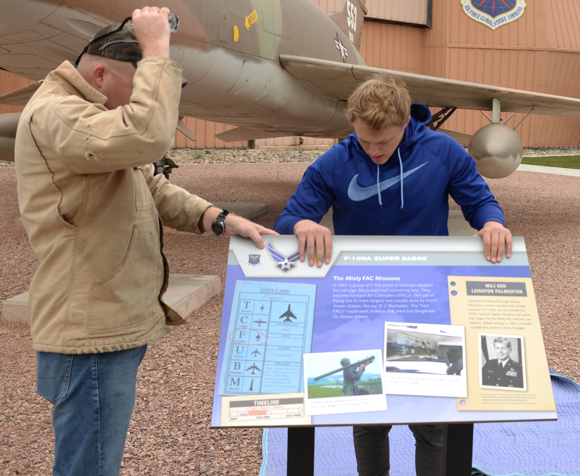 Ryan Ahrenstorff, an eagle scout with Troop 72 from Rapid City, and Master Sgt. Mark Wight, the curator assigned to the South Dakota Air and Space Museum, position a sign in front of an F-100A Super Sabre static display as part of the Adopt-A-Plane Program in Box Elder, S.D., Sept. 23, 2017. Multiple units from Ellsworth Air Force Base and private organizations around the area are adopting aircraft and taking them on as their own by washing, bird proofing and performing minor upkeep. (U.S. Air Force photo by Airman 1st Class Thomas Karol)