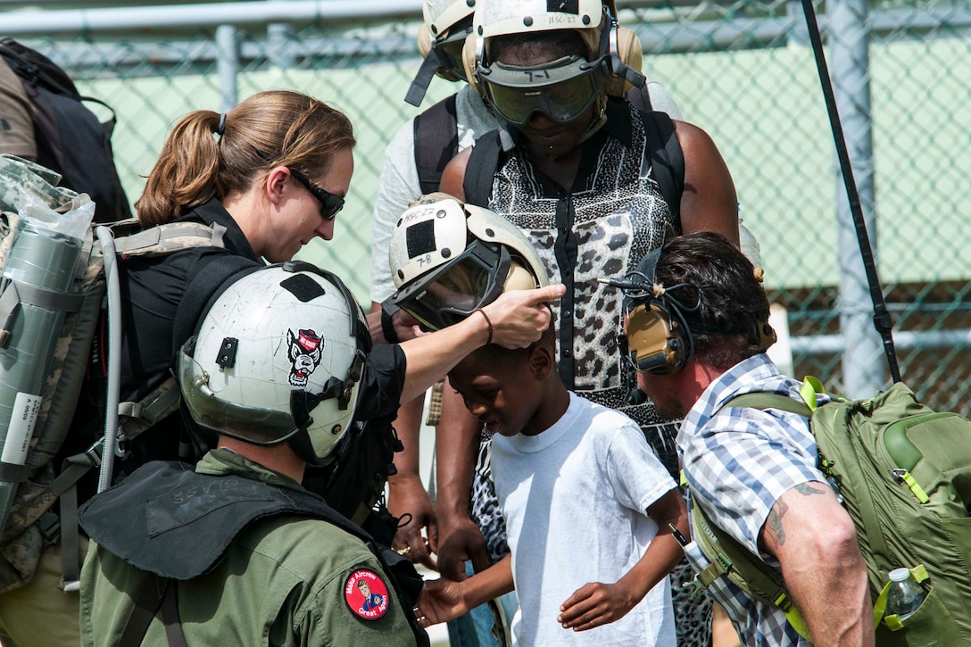 A woman helps put a protective helmet on a child in preparation for helicopter travel.