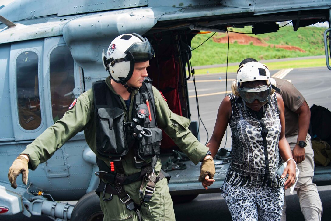 A sailor holds the hand of a civilian while leading her from a helicopter.