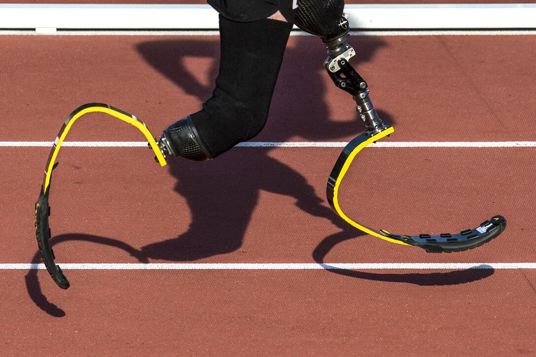 An Army veteran runs with yellow prosthetic legs as his shadow follows.