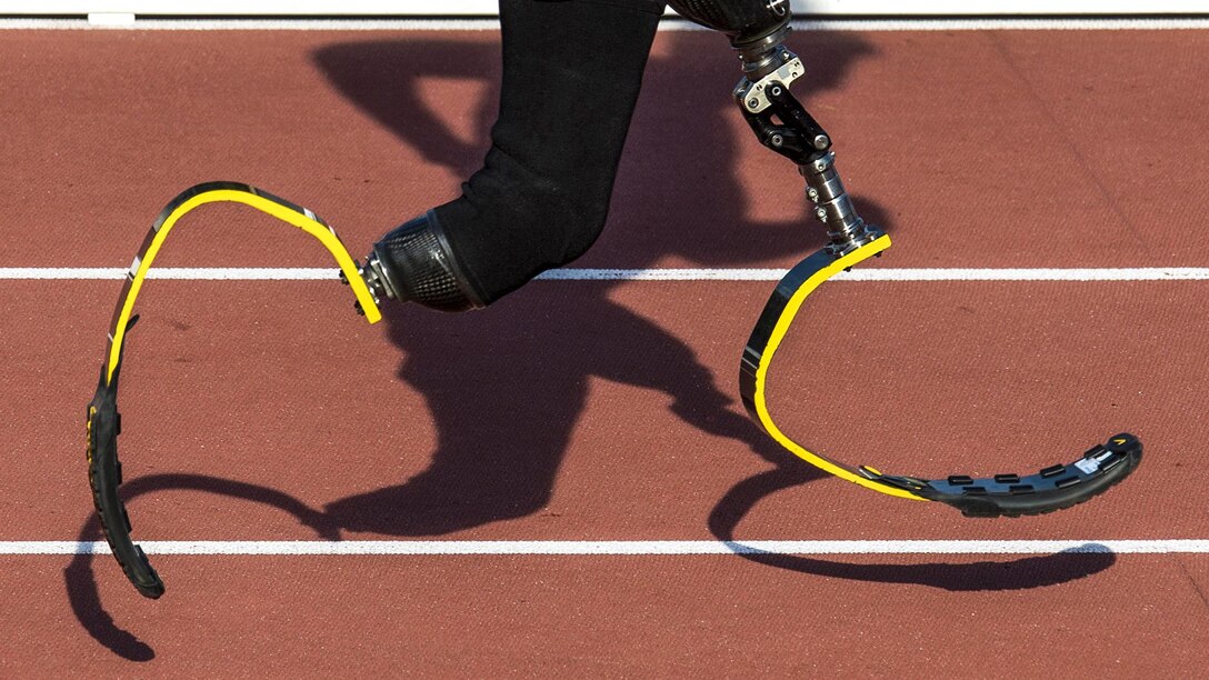 An Army veteran runs with yellow prosthetic legs as his shadow follows.