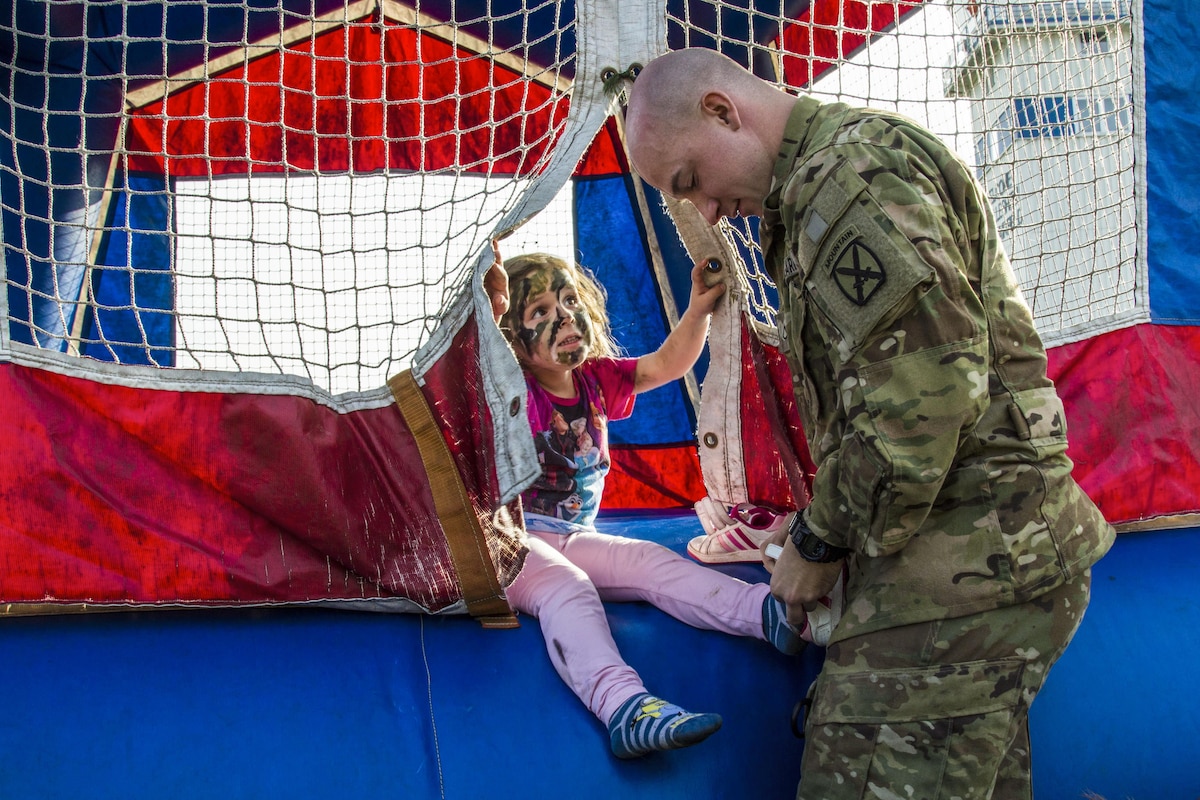 A soldier helps a child put on her shoes.