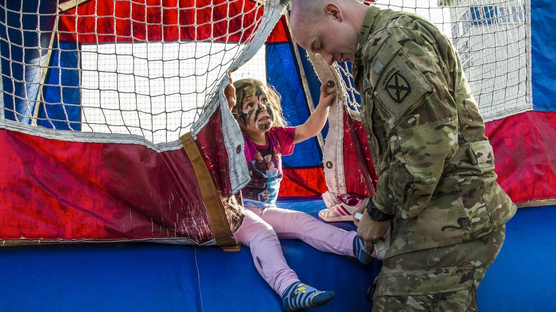 A soldier helps a child put on her shoes.