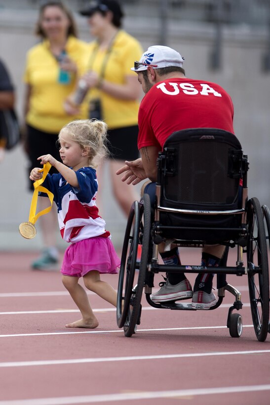 Vada DeWalt, 3, daughter of medically retired Navy Petty Officer 3rd Class Nate DeWalt, right, runs off with her father’s gold medal.