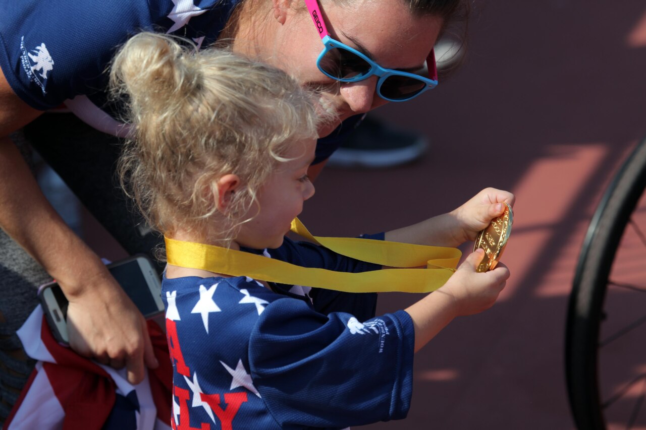 Vada DeWalt, 3, daughter of medically retired Navy Petty Officer 3rd Class Nate DeWalt, shows her mom, Erica, her dad's gold medal