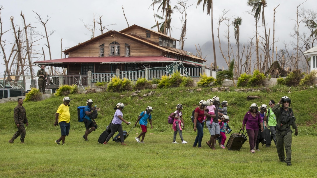 A sailor leads residents with suitcases to a helicopter for evacuation.