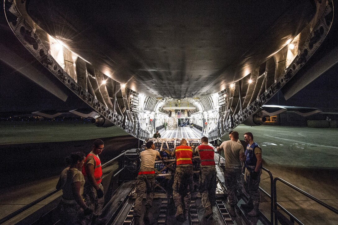 Airmen load palletized food and water onto an aircraft at night.
