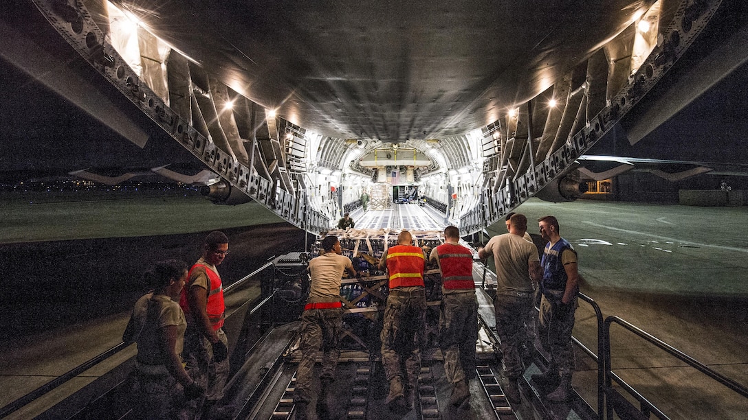 Airmen load palletized food and water onto an aircraft at night.