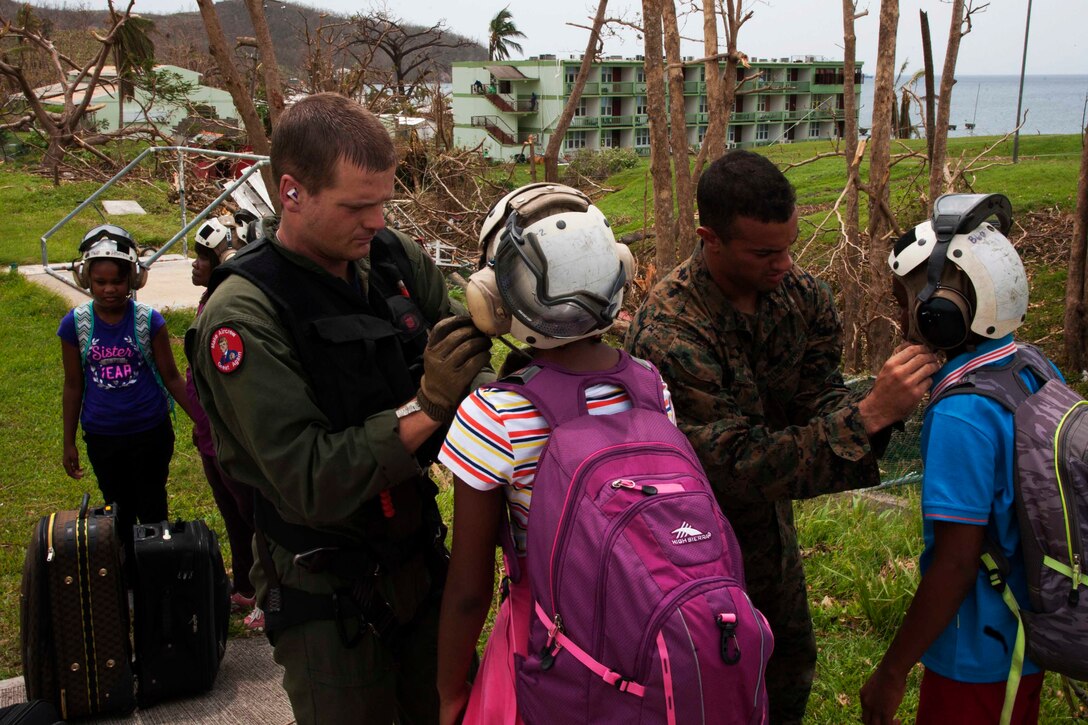 Two sailors help put protective helmets on two young people outside.